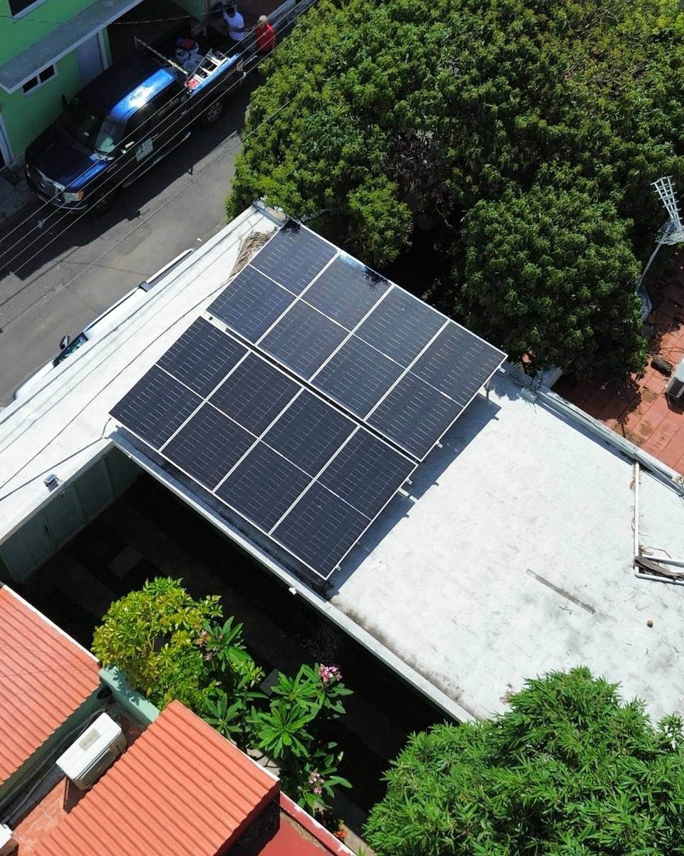 Paneles solares sobre la losa de una casa rodeada de árboles, vista desde dron
