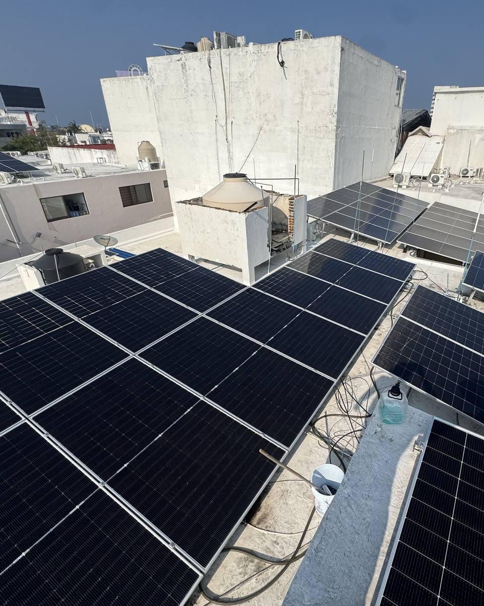 Varios arreglos de paneles solares cubriendo una azotea, entre tinacos y edificios