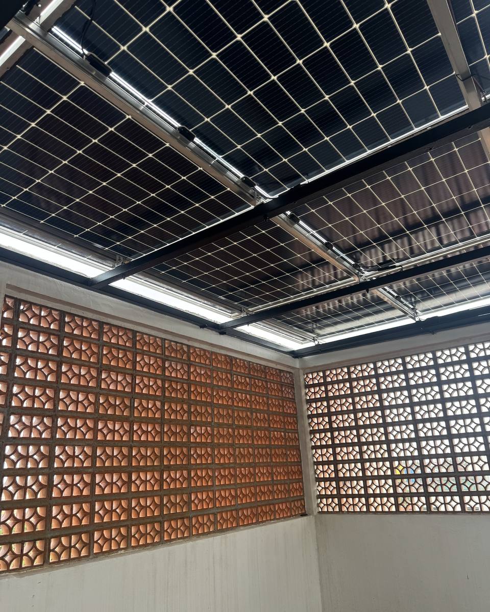 Vista desde abajo de una pérgola de paneles solares sobre una terraza con muro de celosía